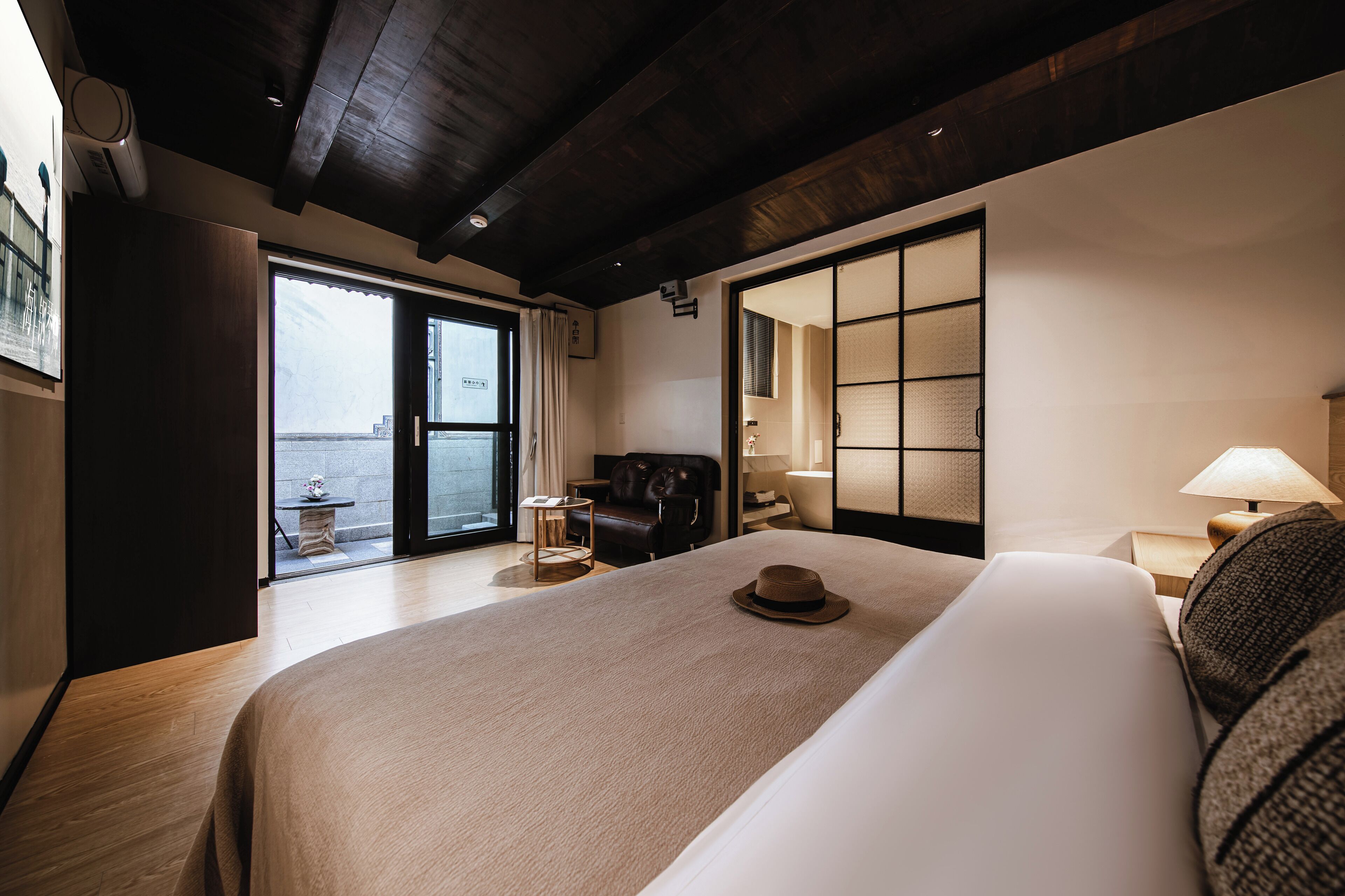 A hotel room with a large bed, a desk, a chair, a lamp, and a view of the outside.