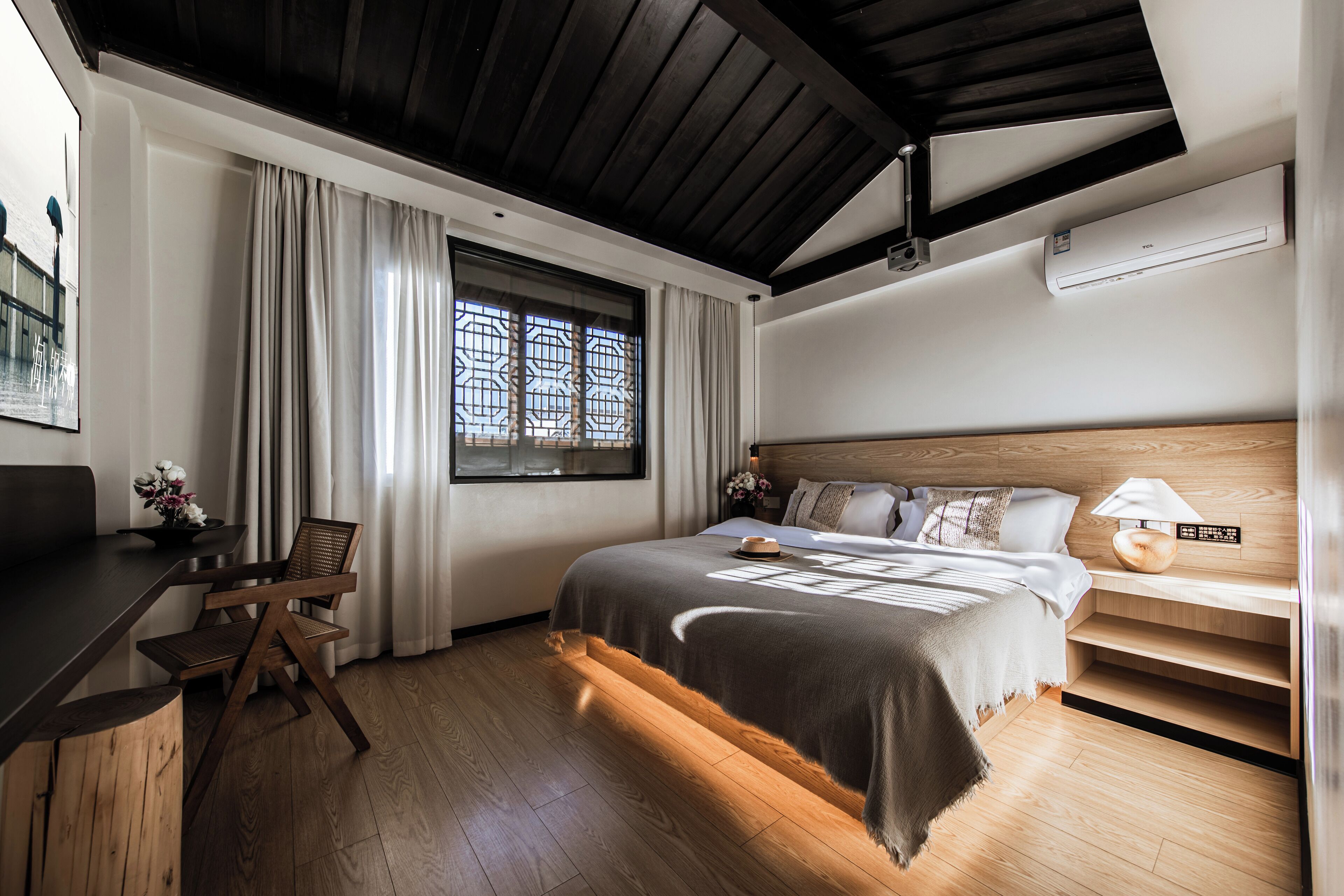 A modern bedroom with a wooden bed, a desk, and a large window with curtains.