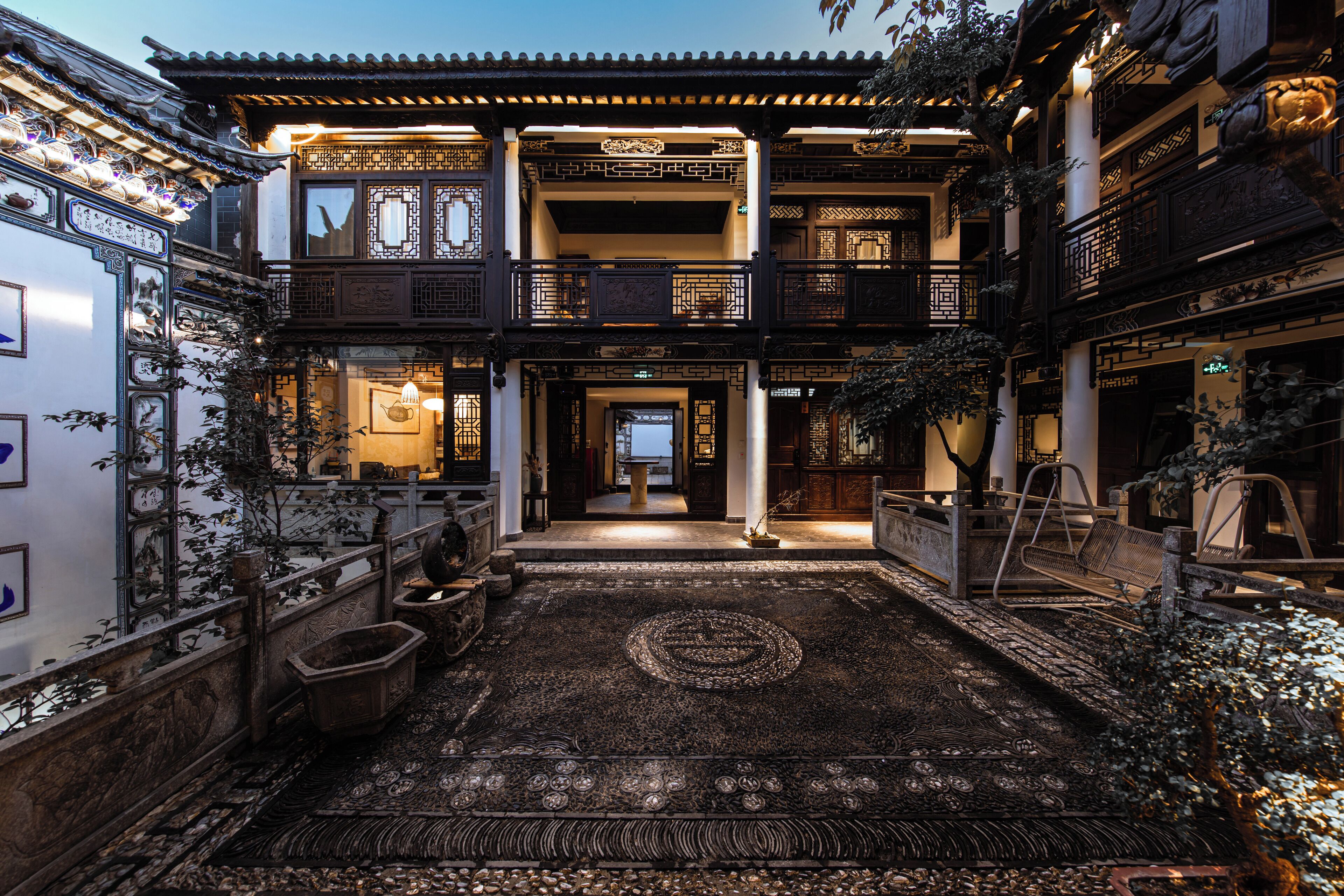 A traditional courtyard with a central circular pattern on the floor, surrounded by ornate railings and potted plants.