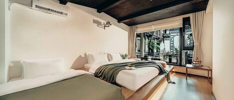 A modern hotel room with a wooden ceiling, a large window with curtains, a bed, a bedside table, and a small balcony.