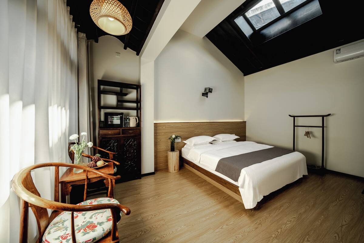 Un dormitorio con cama de madera, un escritorio con silla, una mesita y una ventana con vistas al exterior.
