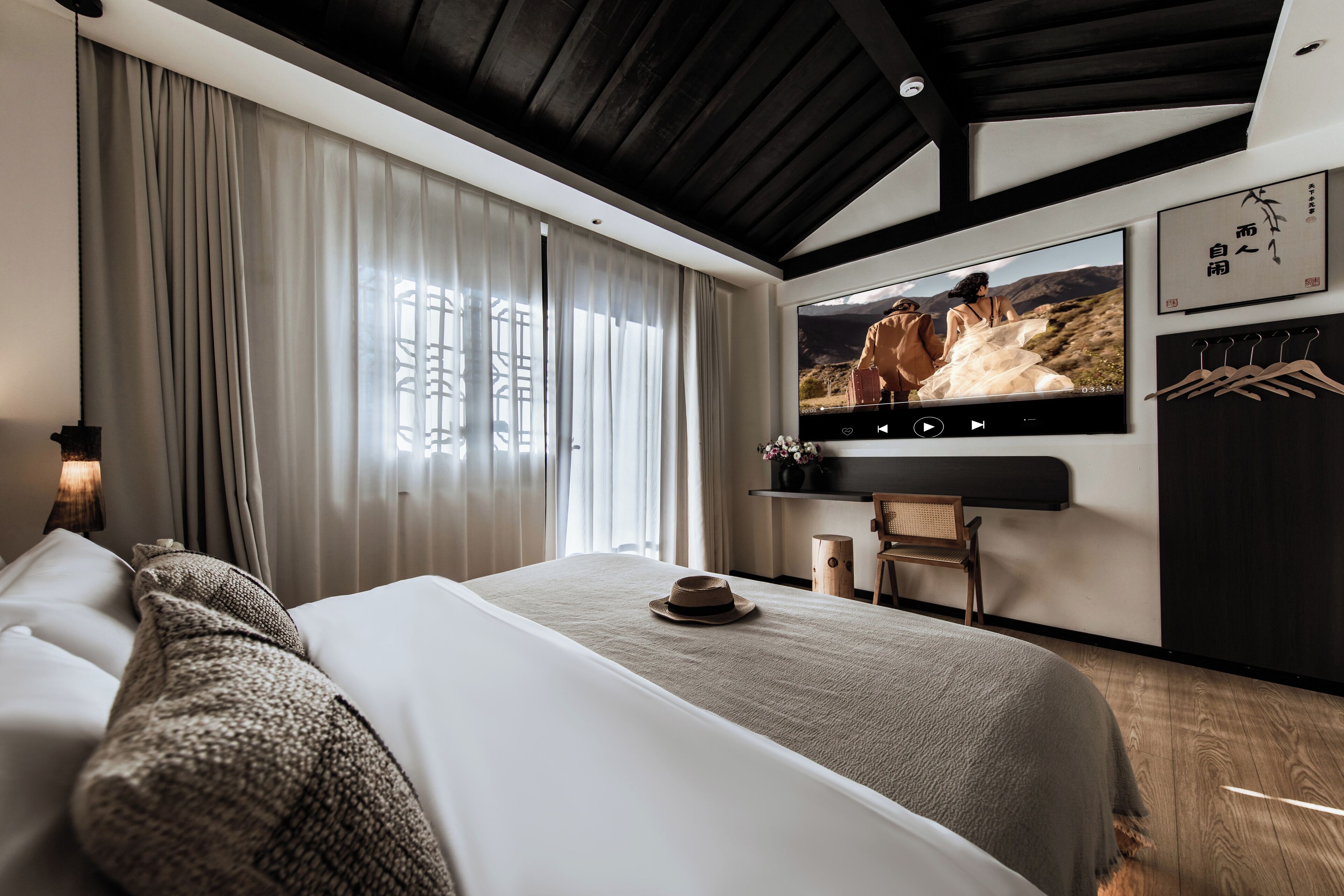 Ein modernes Hotelzimmer mit einem großen Bett, einem an der Wand montierten Fernseher und Blick auf eine gebirgige Landschaft.