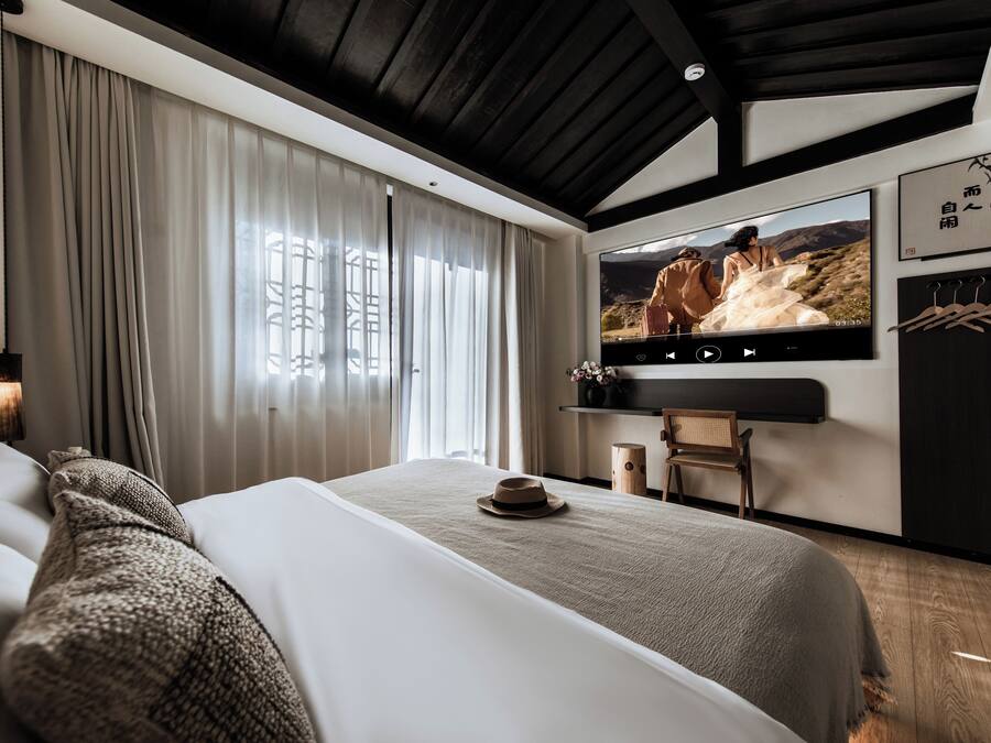 A modern hotel room with a large bed, a television mounted on the wall, and a view of a mountainous landscape.