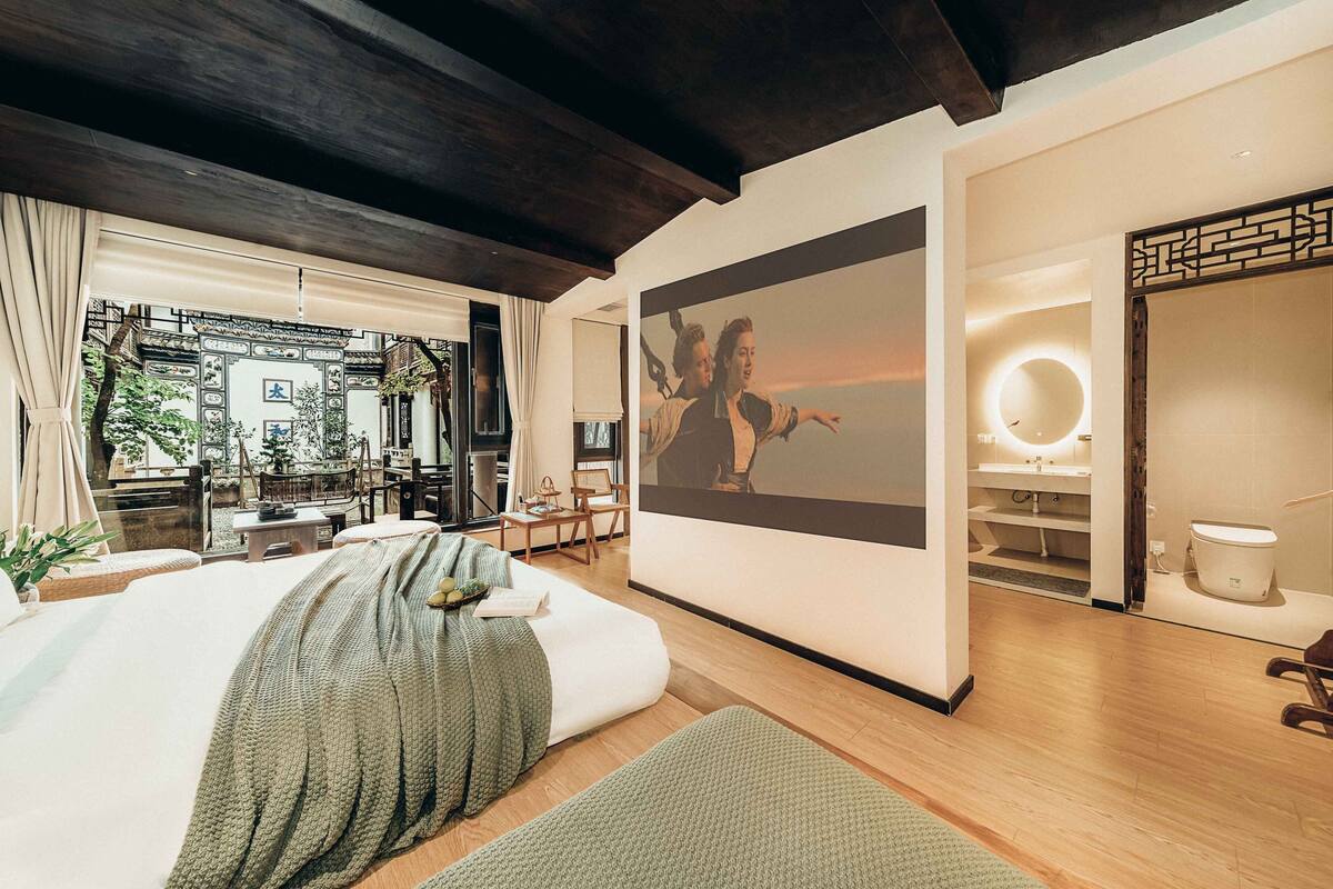 Habitación de hotel moderna con una cama grande, vistas al área exterior, un cuadro en la pared y un baño con un espejo redondo.