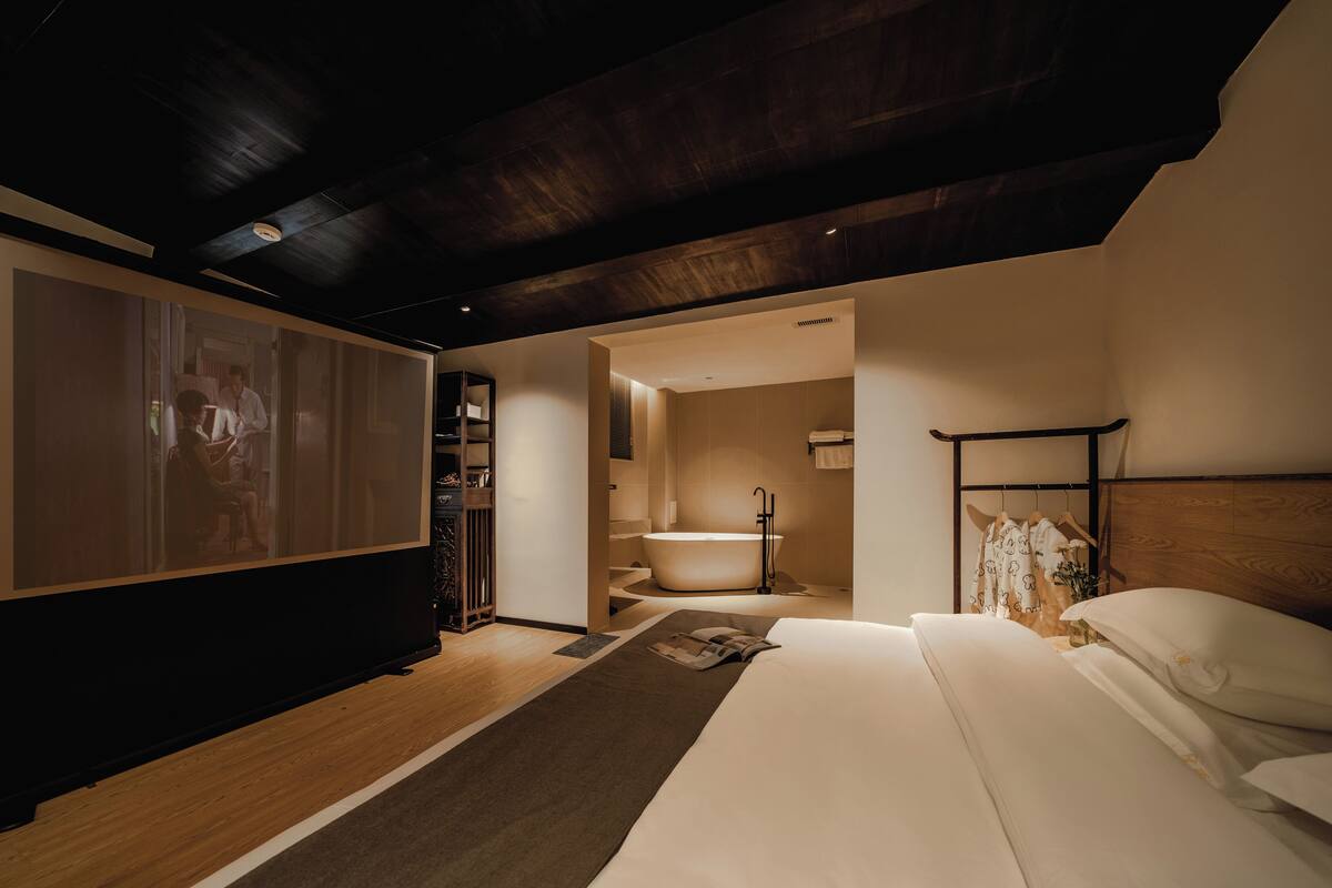 Una habitación de hotel moderna con una cama grande, una bañera y techo de madera.