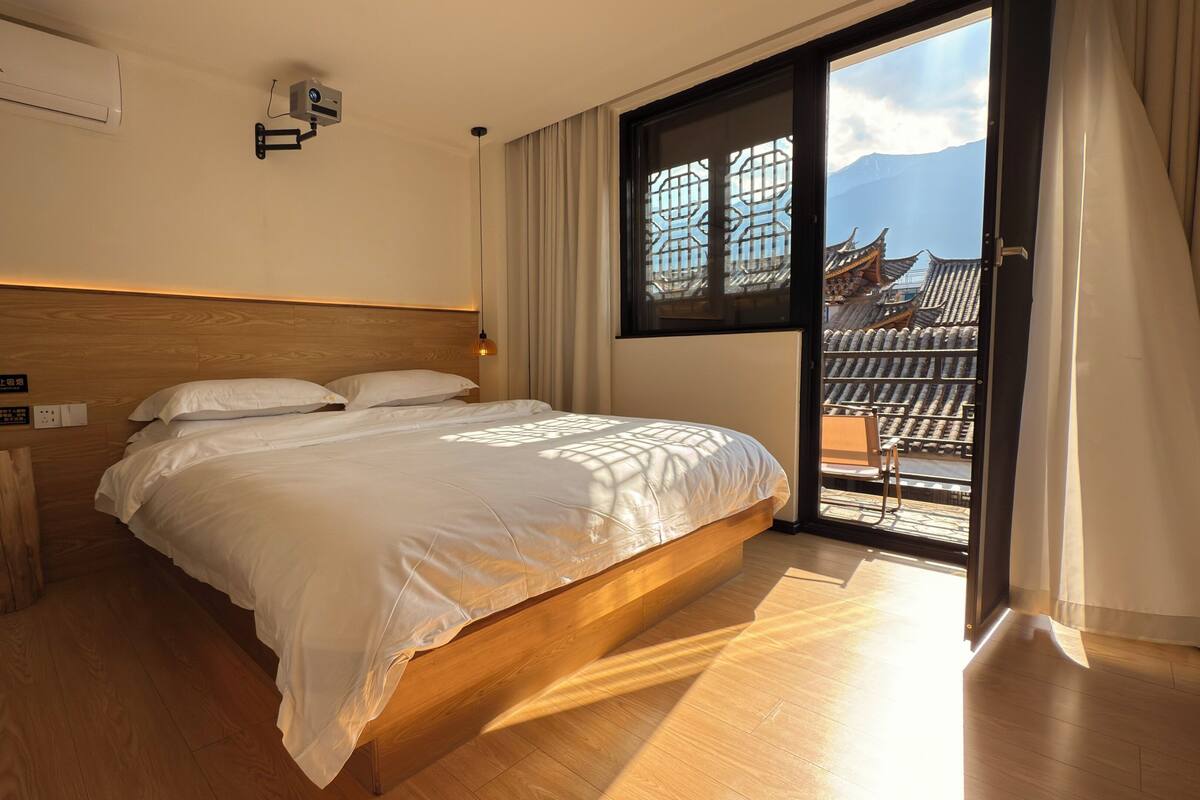 Un dormitorio con cabecera de madera, una cama grande, una ventana con vistas a la arquitectura tradicional y una puerta corredera a un espacio al aire libre.