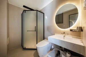 Un baño moderno con cabina de ducha de vidrio, inodoro blanco y tocador con espejo.