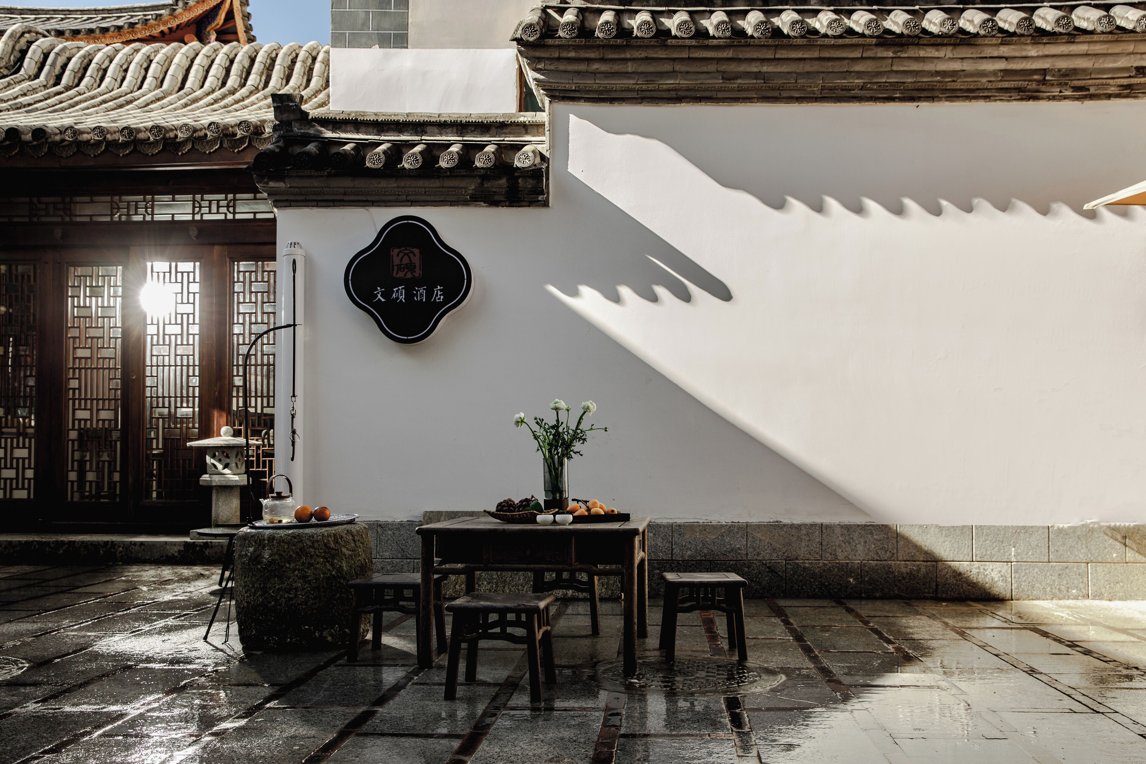 A traditional Chinese courtyard with a tiled floor, a table with a vase of flowers, and a sign with Chinese characters.