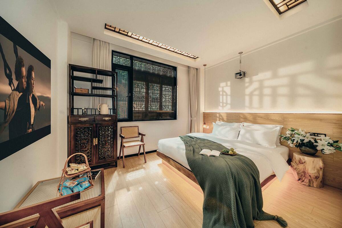 Una habitación de hotel moderna con una cama grande, una mesita de noche de madera, un escritorio con una silla, una ventana con vistas y un cuadro en la pared.