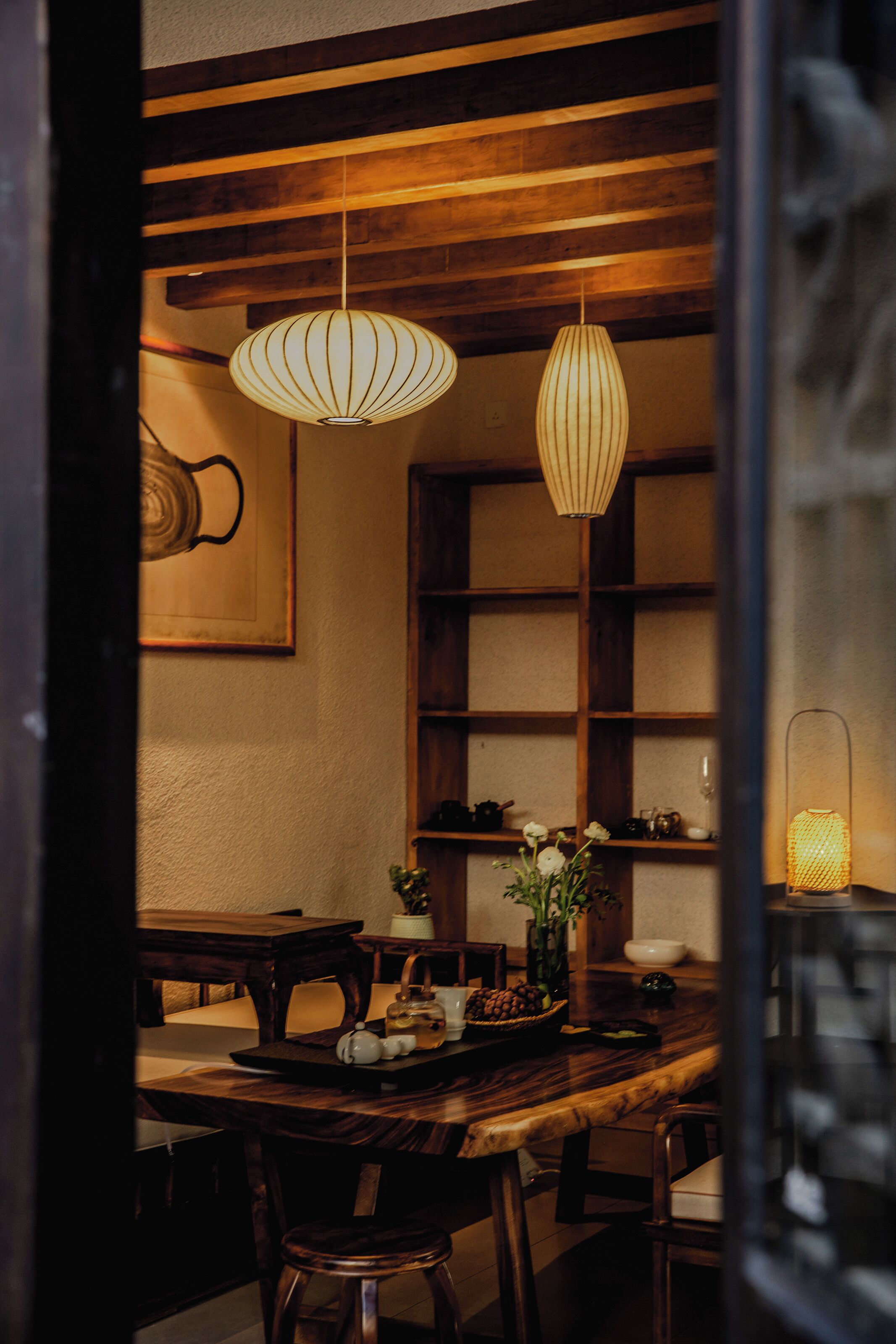A dining area with wooden furniture, hanging pendant lights, and a vase with flowers.