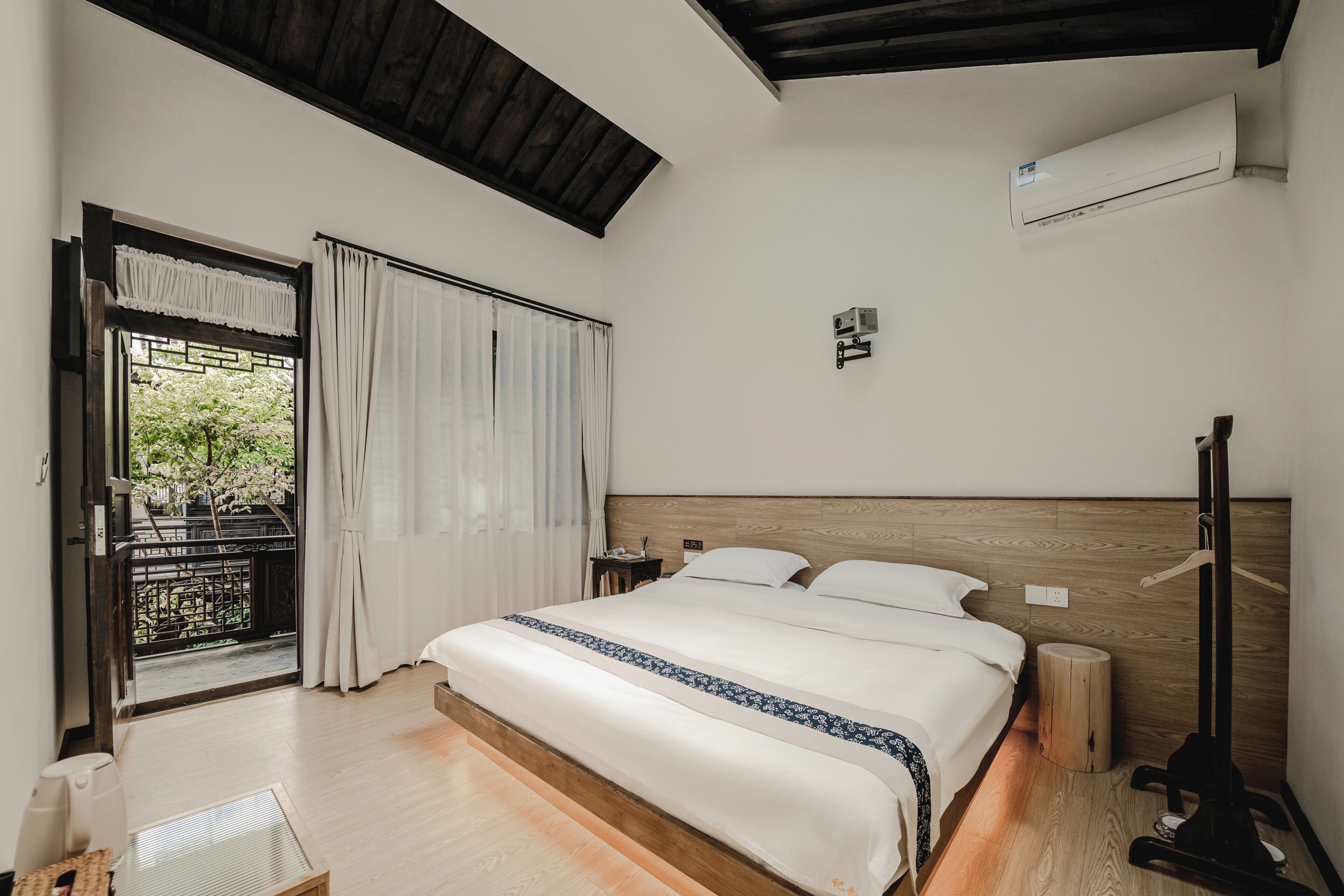 Ein Schlafzimmer mit einem großen Bett, einem Holzkopfteil, einem Nachttisch, Vorhängen an einem Fenster und einer Klimaanlage.