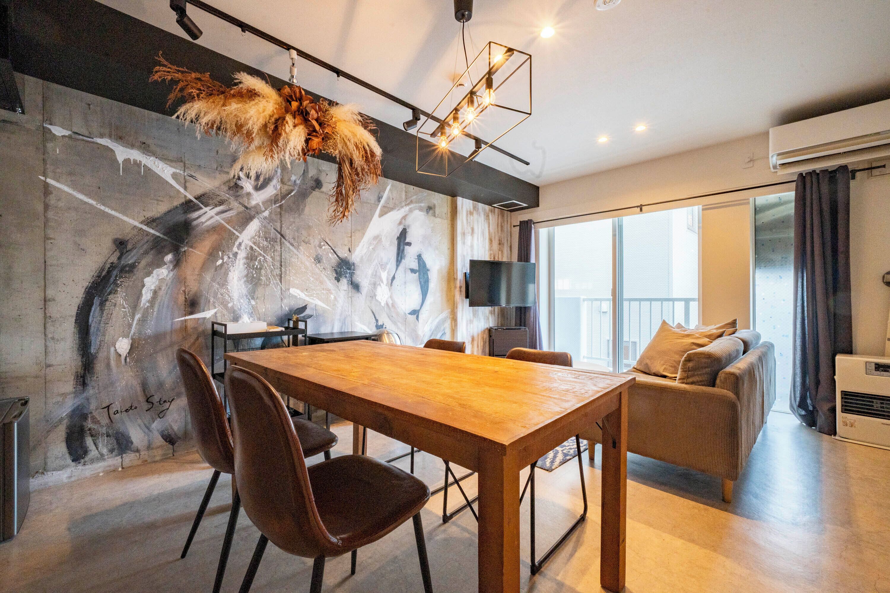 A modern dining area with a wooden table and chairs, a large abstract painting on the wall, and a sofa in the adjacent living area.