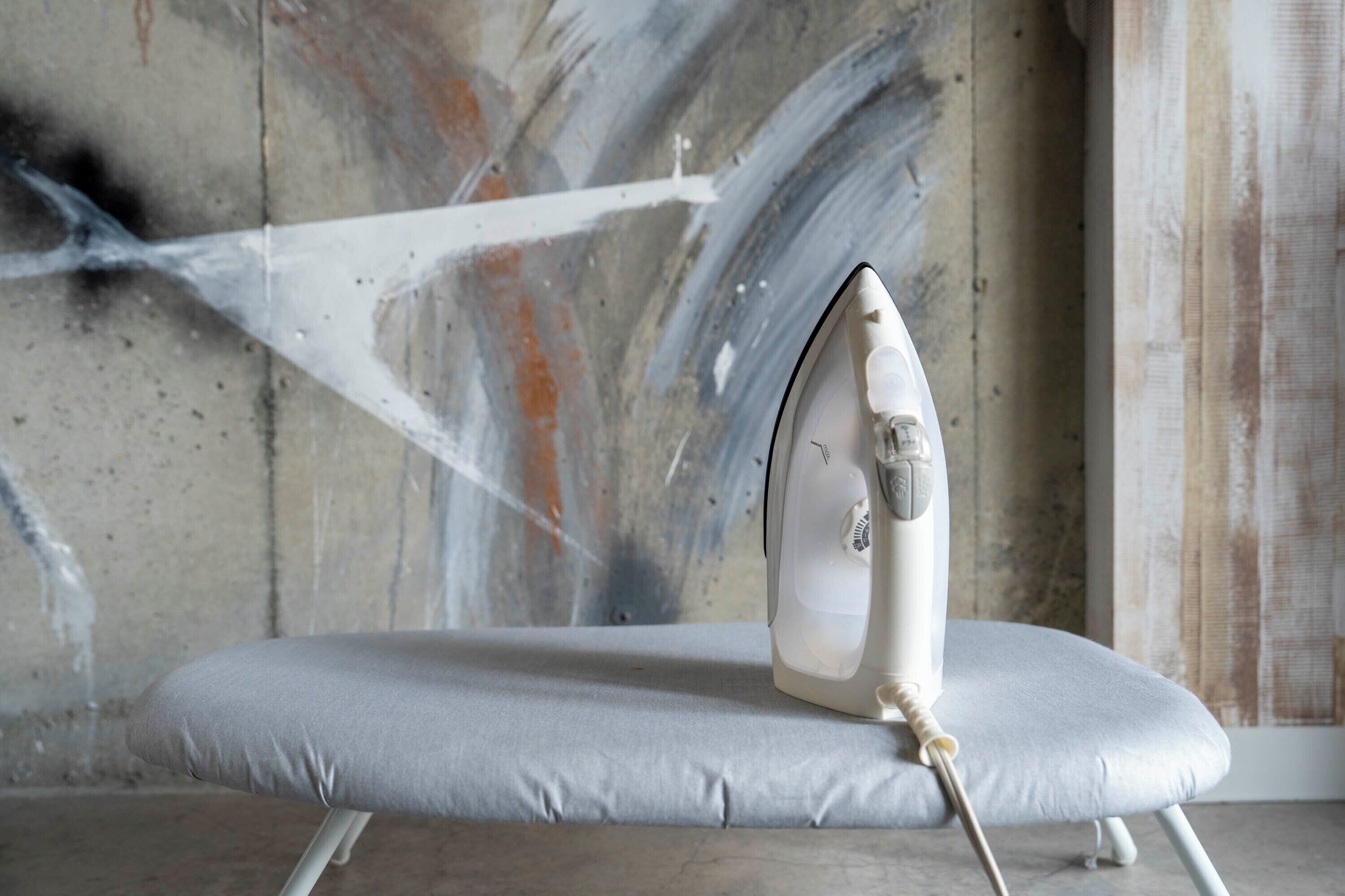 A white ironing board with an iron on top, placed against a wall with abstract art.