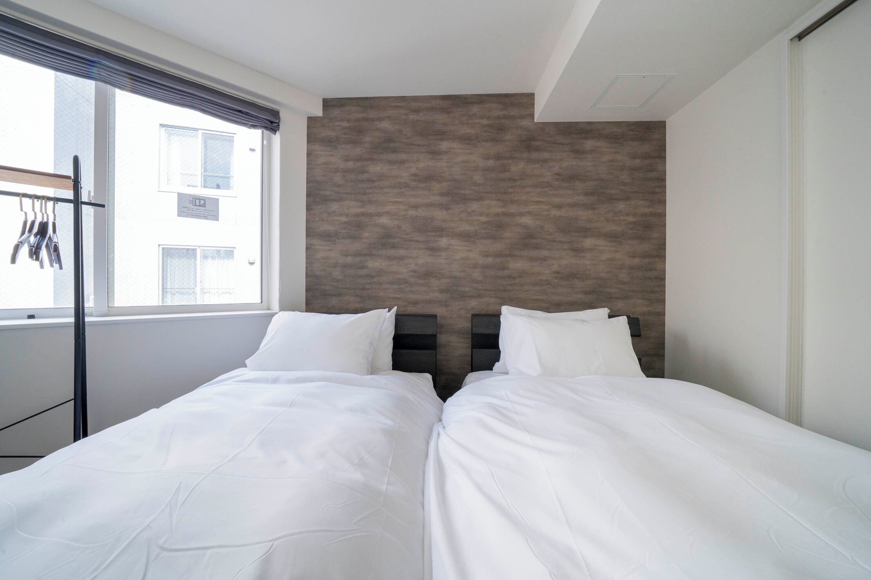 A twin room with two beds, a window with a view of buildings, and a wall with a textured pattern.