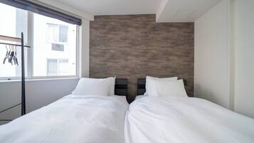 A twin room with two beds, a window with a view of buildings, and a wall with a textured pattern.