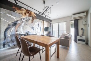 A modern living room with a wooden dining table, brown chairs, a sofa, and a large abstract painting on the wall. - TAKETO STAY KOTONI  202 (Sapporo)