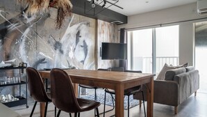 Ein modernes Wohnzimmer mit einem Holzespeisetisch, zwei braunen Ledersesseln, einem grauen Sofa und einem großen, abstrakten Gemälde an der Wand.