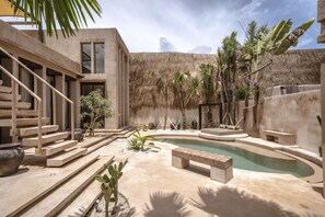 Un espace piscine extérieur moderne doté d’un toit de chaume, d’escaliers en béton et de mobilier minimaliste.