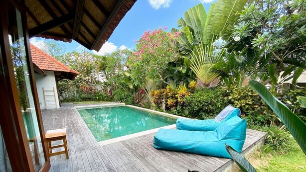 A wooden deck with a pool, a blue lounge chair, and lush tropical vegetation. - Villa Kevin - 3BR Private Villa (Kecamatan Mengwi)
