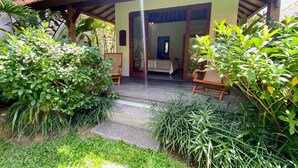 A wooden structure with a covered porch, a dining area with chairs, and a view into the interior. - Villa Kevin - 3BR Private Villa (Kecamatan Mengwi)