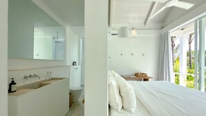 A modern bathroom with a large sink and mirror, a separate toilet, and a bedroom with a bed and a window with curtains. - Villa Atara - 2BR Premium Private Pool Villa Pererenan (Kecamatan Mengwi)