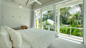 A bedroom with a large bed, a ceiling fan, and a view of lush greenery through large windows. - Villa Atara - 2BR Premium Private Pool Villa Pererenan (Kecamatan Mengwi)