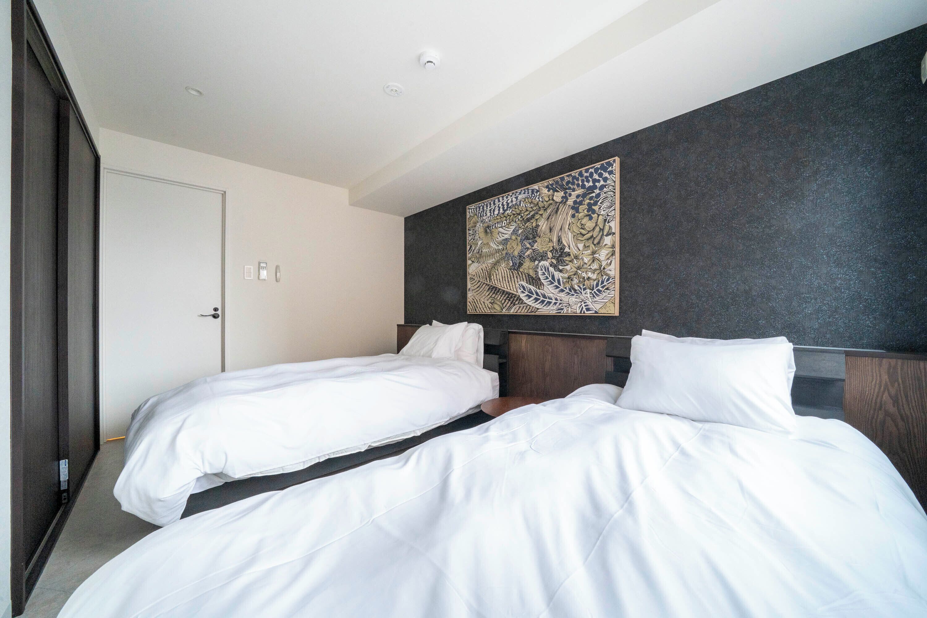 Ein Hotelzimmer mit zwei Einzelbetten, einer dunkel strukturierten Wand und einem großen dekorativen Kunstwerk darüber.