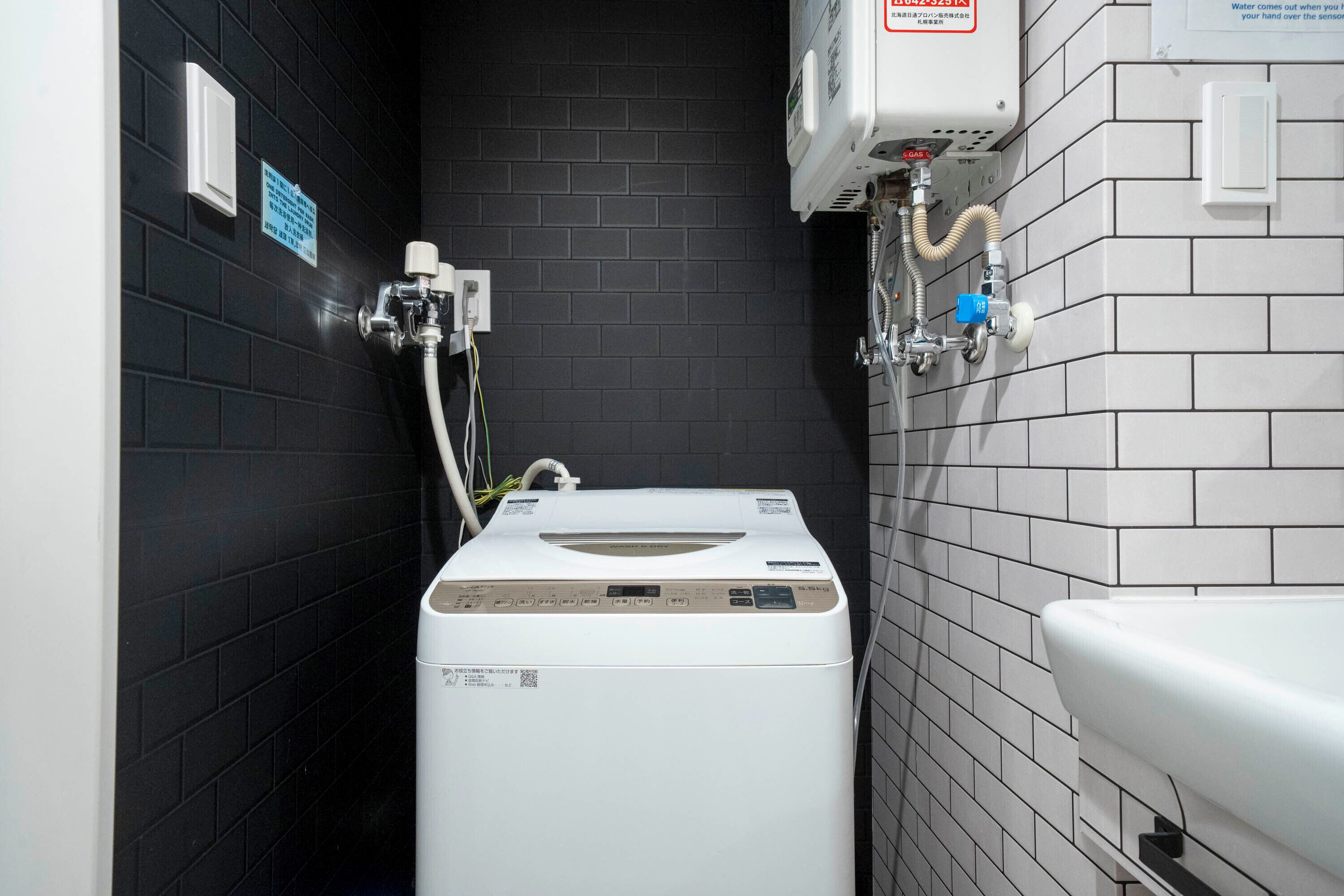 A compact, modern bathroom with a black tiled wall, a white sink, and a built-in washing machine.