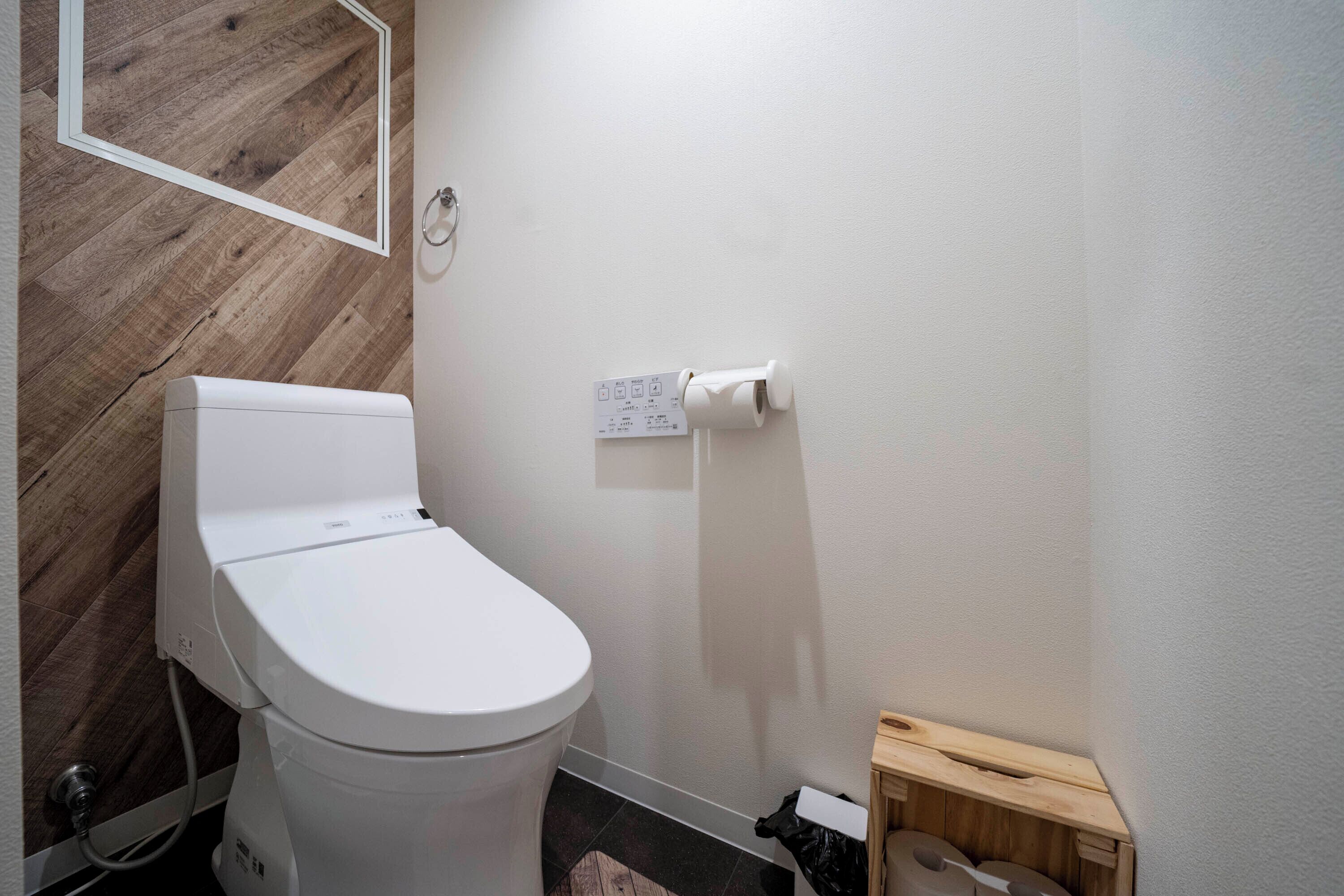 Un baño moderno con inodoro blanco, paneles de madera en la pared, un dispensador de papel higiénico y un pequeño armario de madera.