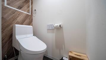 Un baño moderno con inodoro blanco, paneles de madera en la pared, un dispensador de papel higiénico y un pequeño armario de madera.