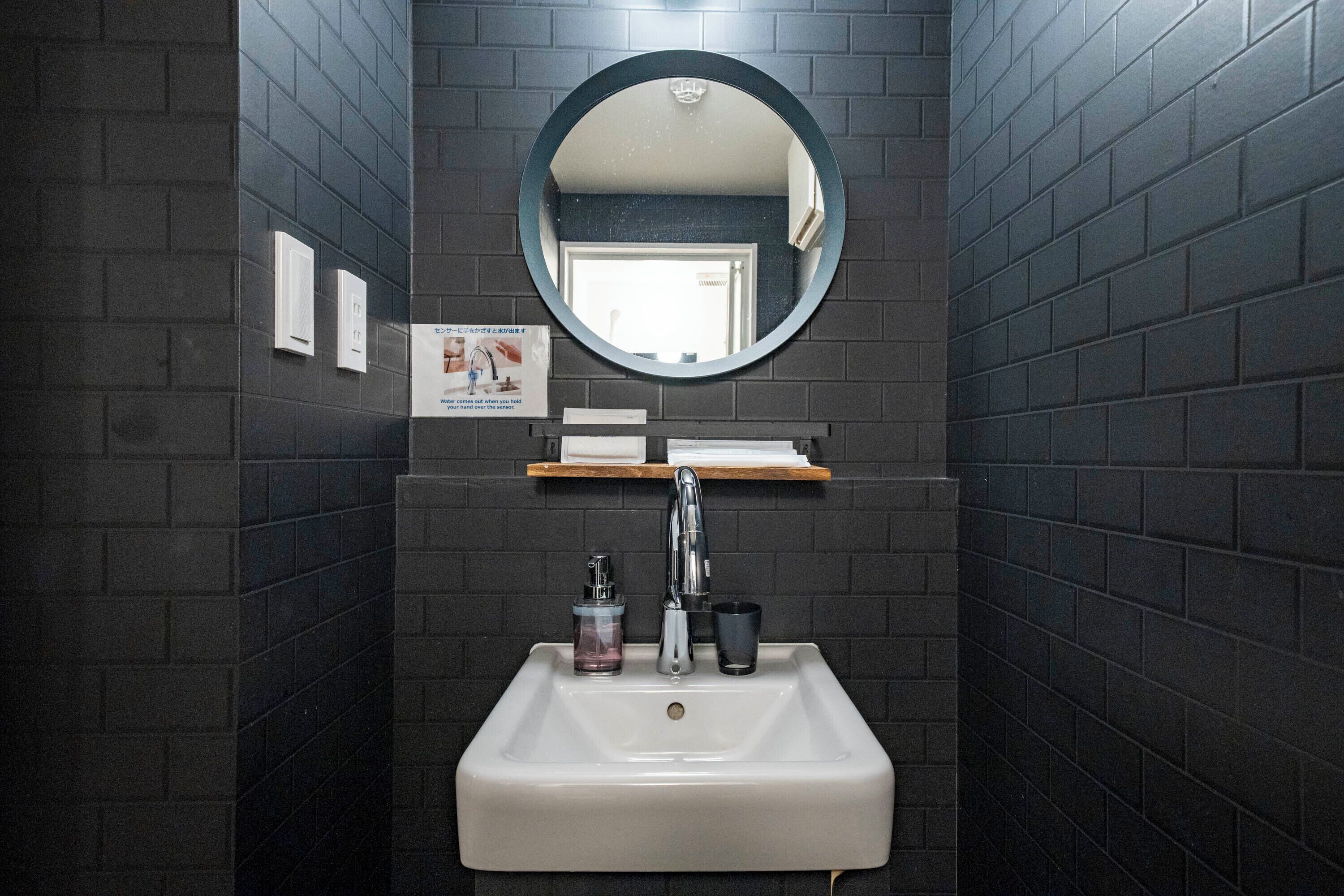 A bathroom with a white sink, a round mirror, and a dark tiled wall.