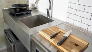 Keittiössä on ruostumattomasta teräksestä valmistettu pesuallas, kannettavalla liedellä oleva paistinpannu ja puinen leikkuulauta, jonka päällä on veitsi.