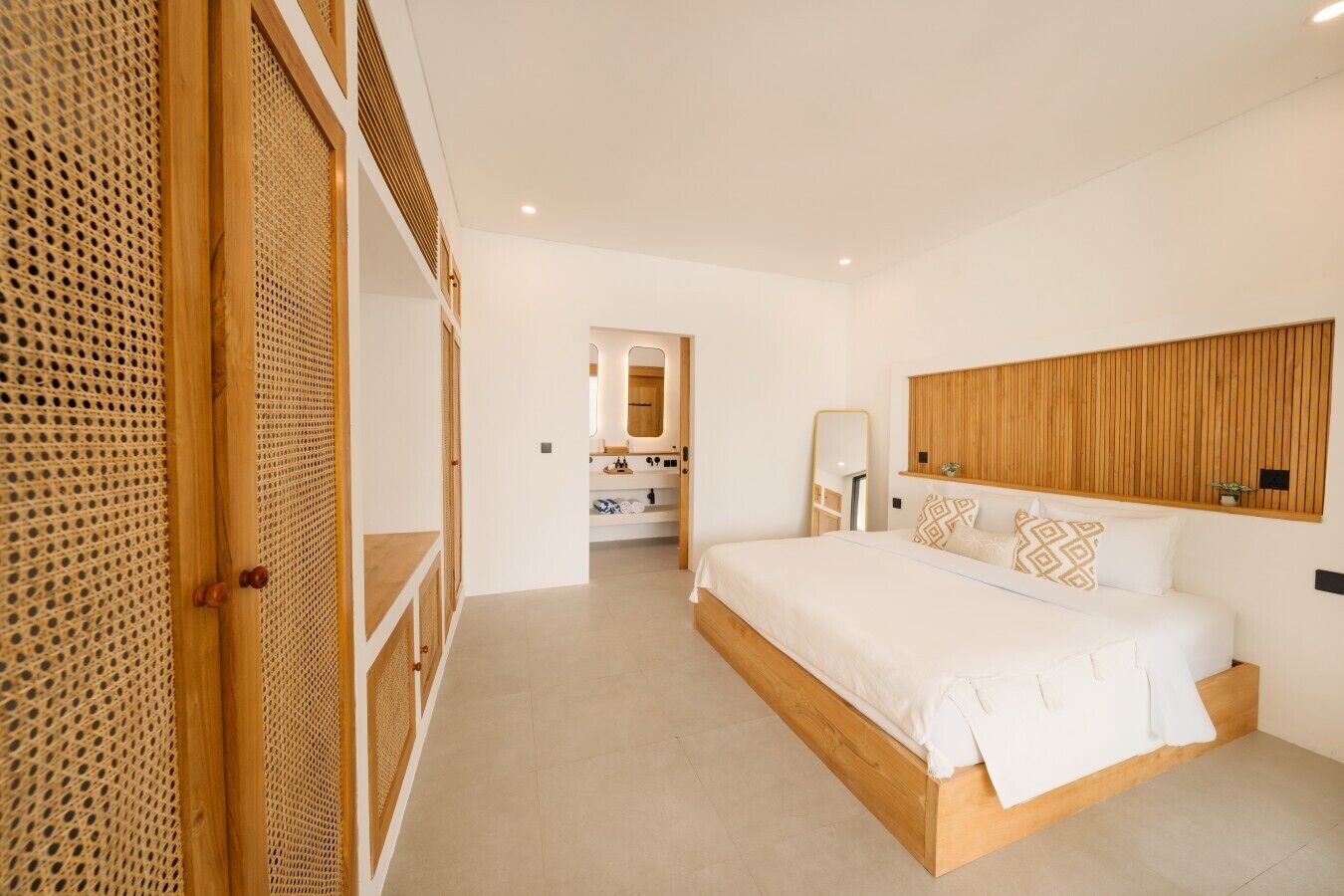 A modern bedroom with a large bed, a wooden headboard, and a walk-in closet with a woven door.