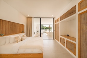 A modern bedroom with a large bed, a wooden headboard, a TV, and a sliding glass door leading to an outdoor area.