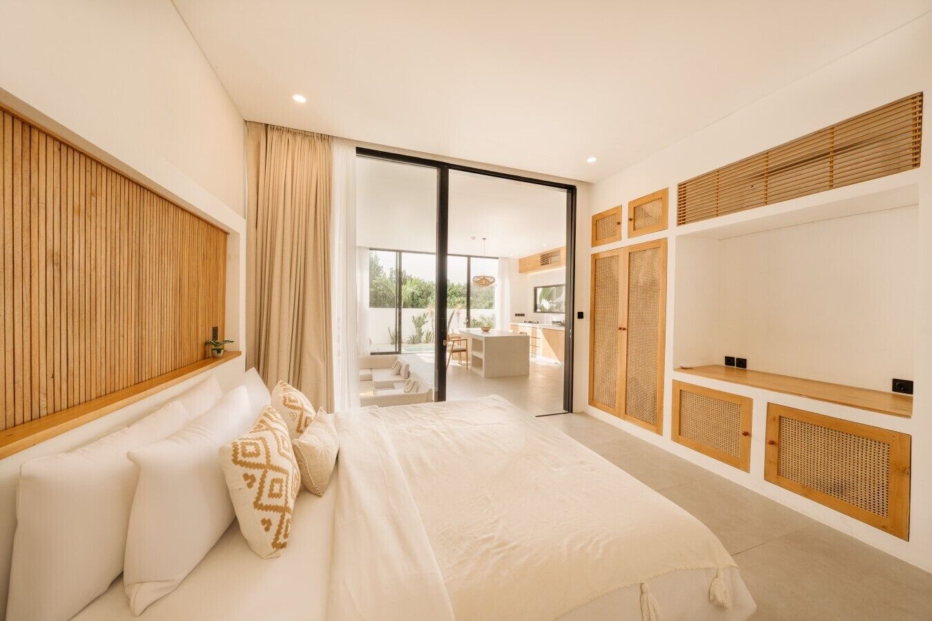 Ein modernes Schlafzimmer mit einem großen Bett, einer Schiebeglastür, die auf einen Balkon führt, und einem eingebauten TV-Regal.