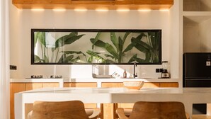 Una cocina moderna con una isla central, sillas de madera y un amplio ventanal con vista a plantas.