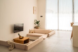 A modern living room with a sofa, a flat-screen TV, a small wooden table with fruit, and a potted plant. - Alcove Boutique Private Pool Villa D (Kecamatan Kuta Selatan)