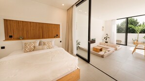 A modern bedroom with a large bed, a wooden headboard, and a sliding glass door leading to a balcony with outdoor furniture. - Alcove Boutique Private Pool Villa D (Kecamatan Kuta Selatan)