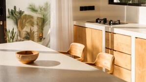 A modern kitchen with wooden cabinets, a white countertop, and a dining area with two wooden chairs and a bowl. - Alcove Boutique Private Pool Villa D (Kecamatan Kuta Selatan)
