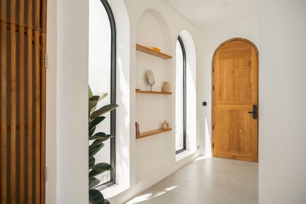 A hallway with arched windows, wooden shelves, and a wooden door. - Alcove Boutique Private Pool Villa D (Kecamatan Kuta Selatan)