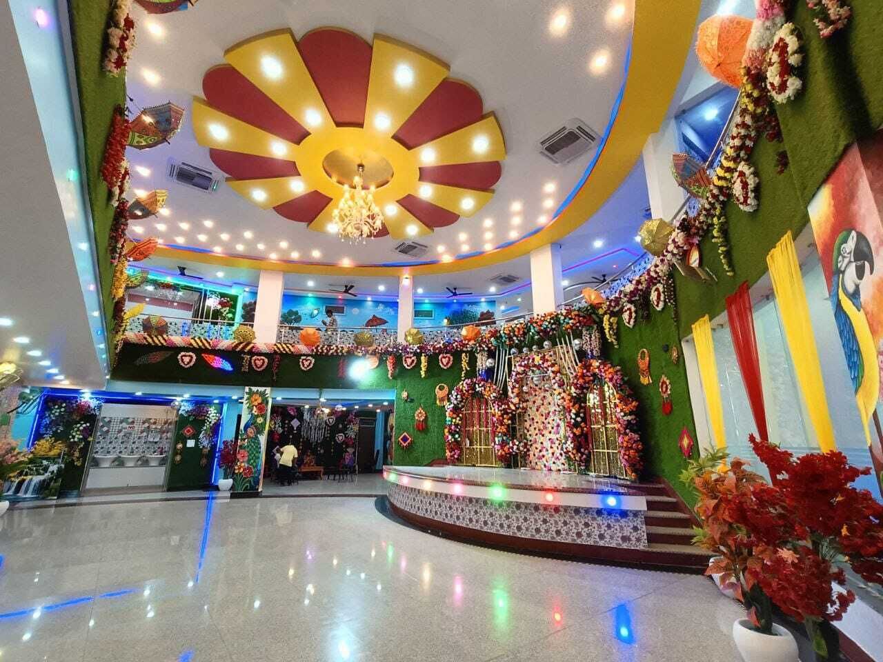 Un atrio bien iluminado con un escenario central, arreglos florales decorativos y un techo con un diseño de luces radiales.