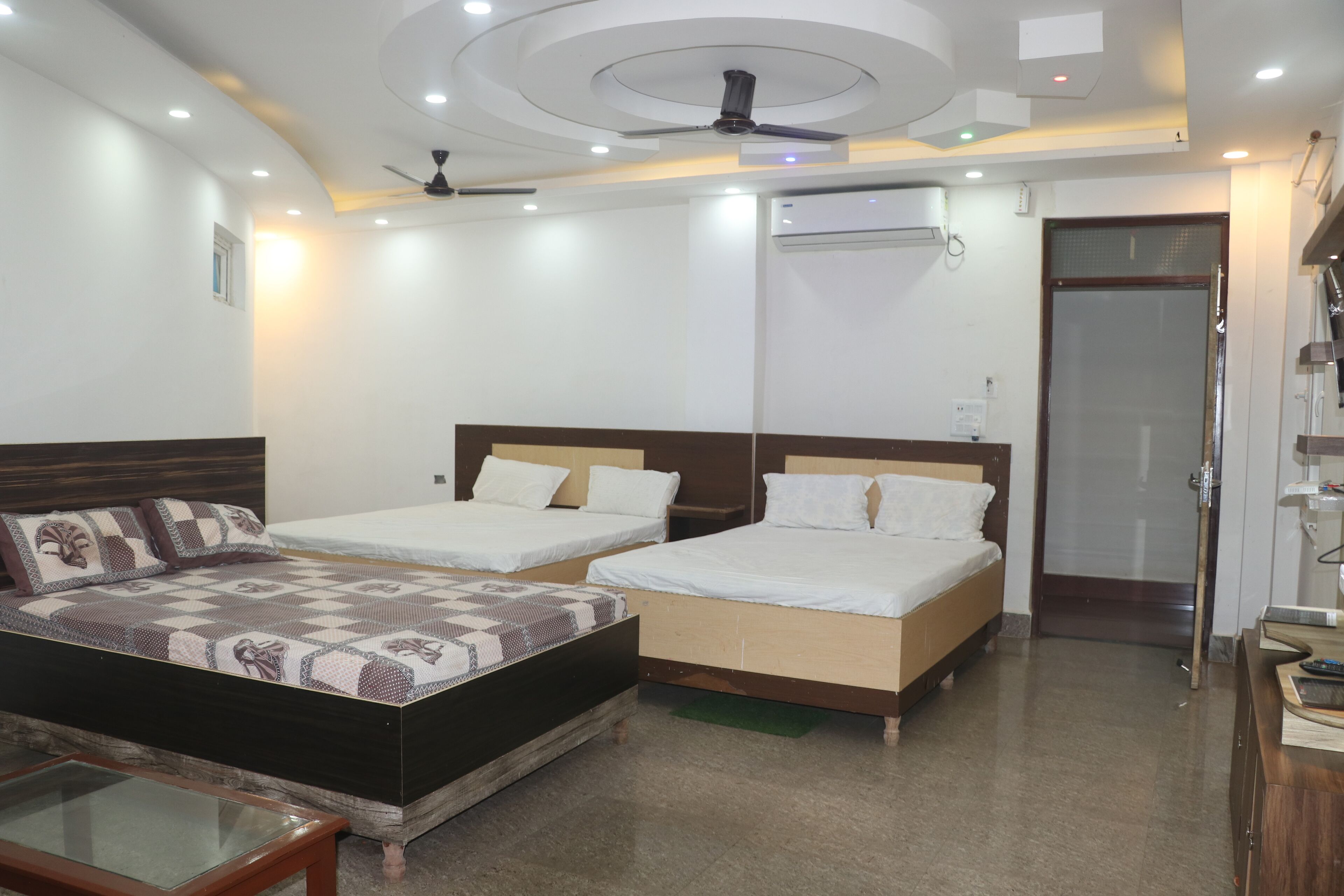 Une chambre d’hôtel avec deux lits simples, un grand lit, une table basse en verre, un ventilateur de plafond et un appareil de climatisation.
