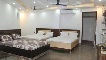 A hotel room with two single beds, a large bed, a glass coffee table, a ceiling fan, and an air conditioning unit.