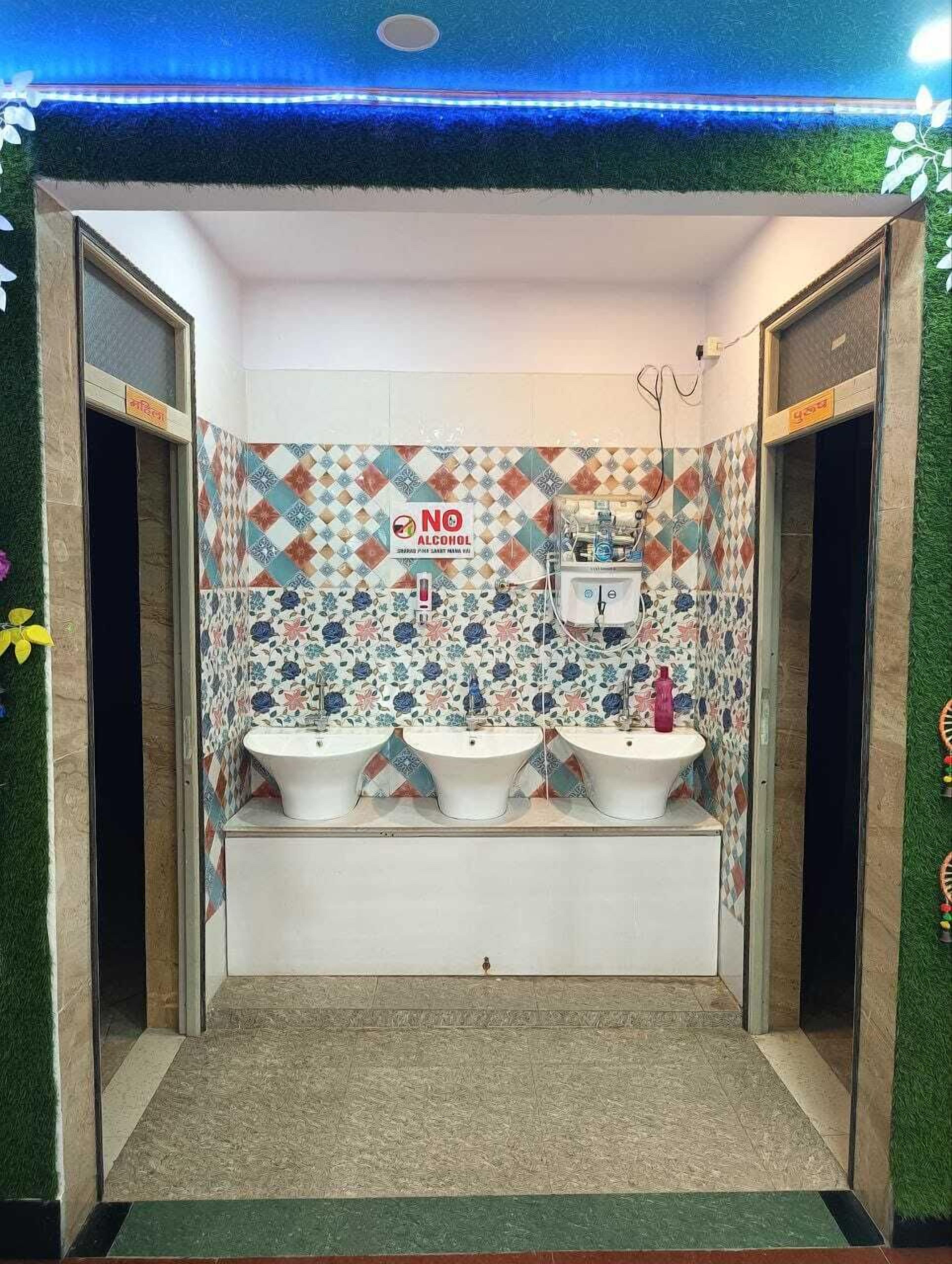 A restroom with three sinks, a 'NO ALCOHOL' sign, and a patterned tile wall.