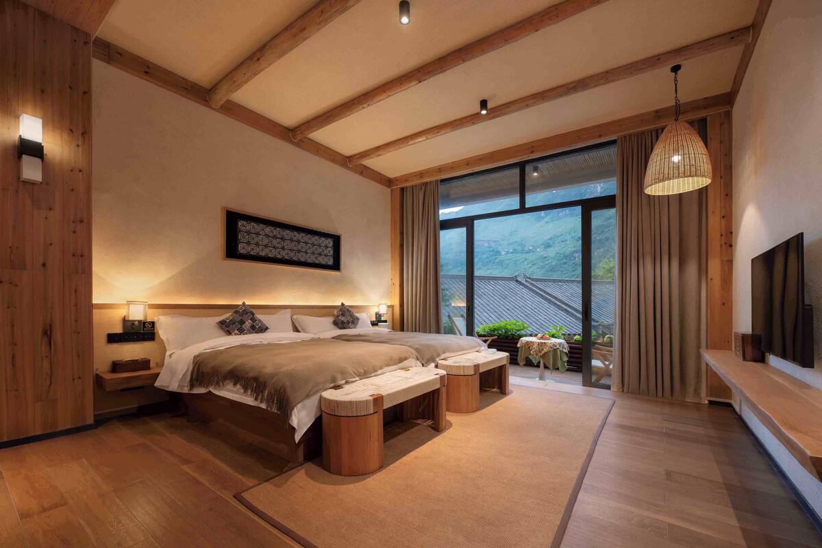 Un dormitorio moderno con una cama grande, cabecera de madera, mesitas de noche, televisor montado y un ventanal con cortinas.