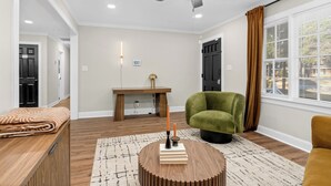 A modern living room with a ceiling fan, a round wooden coffee table, a green armchair, and a window with blinds.