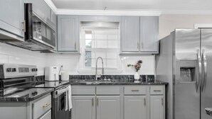 A modern kitchen with grey cabinets, stainless steel appliances, and a marble countertop.