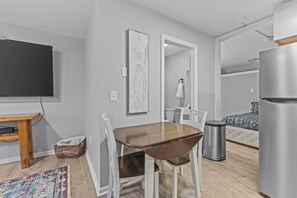 Ein kompakter Wohnraum mit Esstisch, Stühlen, Fernseher, Sofa und Kühlschrank.