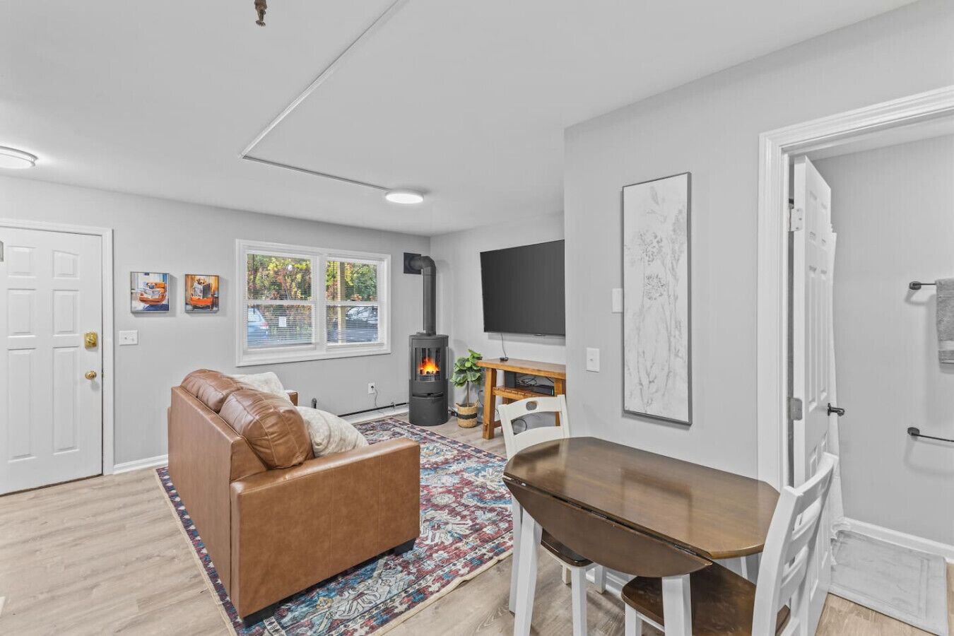 A modern living room with a brown leather sofa, a wooden dining table, a fireplace, a TV, and artwork on the walls.