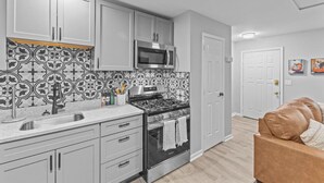 Una cocina moderna con armarios blancos, un salpicadero blanco y negro, electrodomésticos de acero inoxidable y encimera de madera.